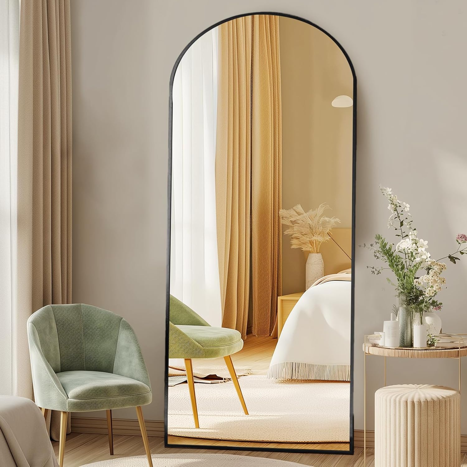 Full-length black arched floor mirror leaning against a wall